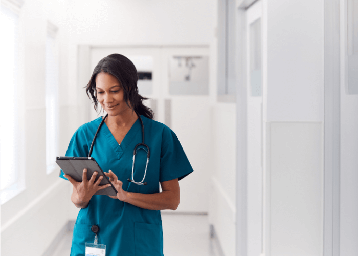Nurse walking in clinical setting looking at a tablet