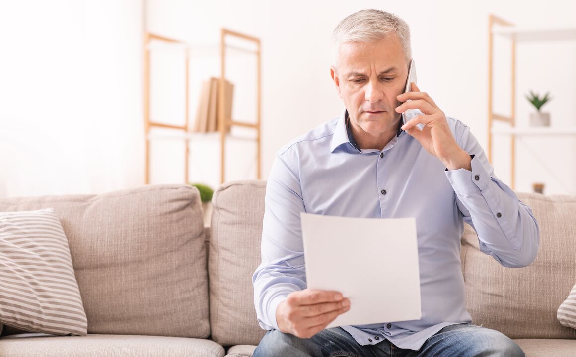 Older man with gray hair speaking on the phone while reviewing a document.