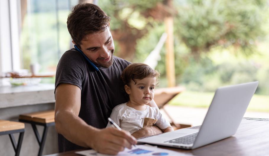 Father holding his son while working remotely
